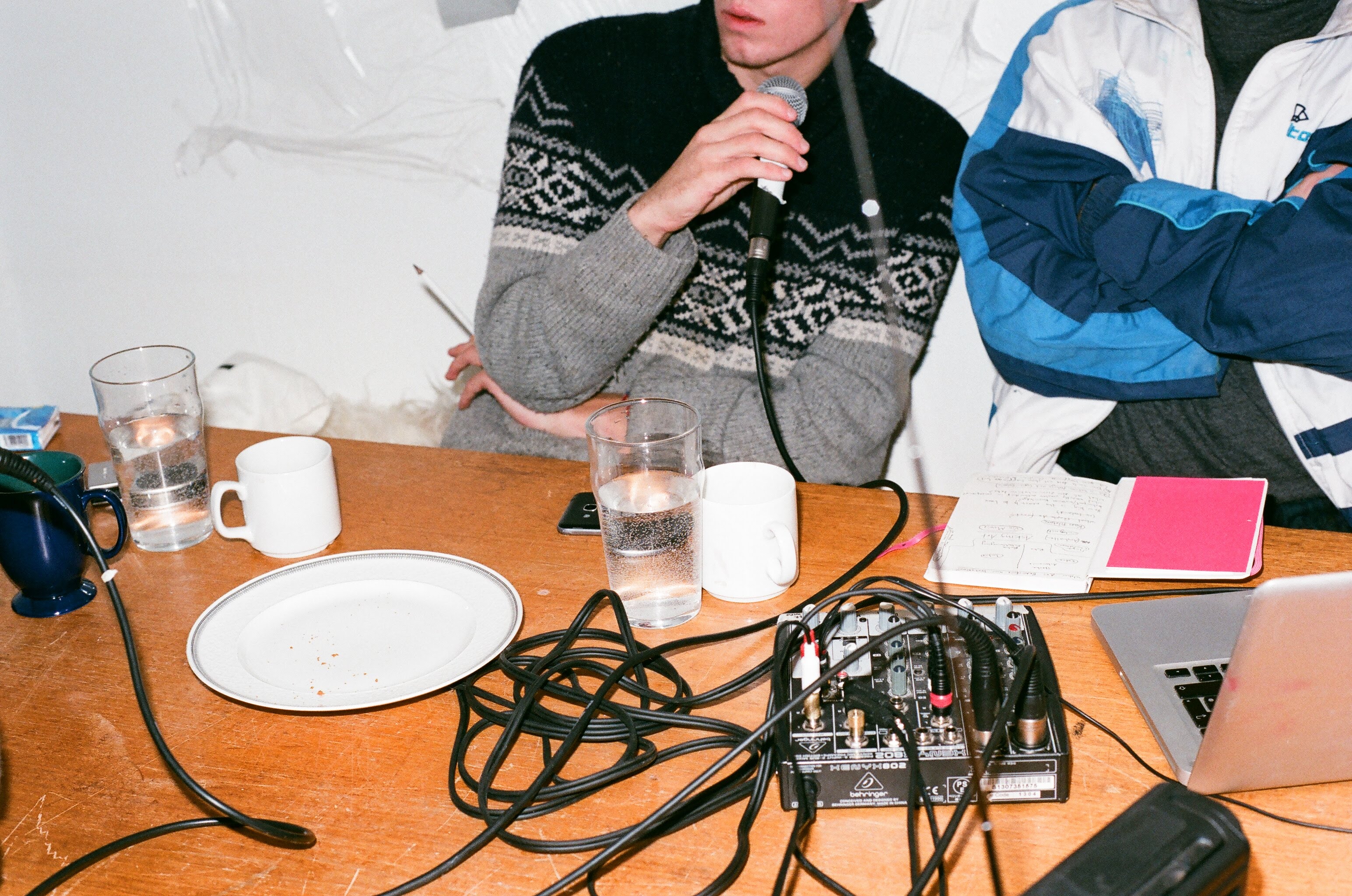 Two people are sitting at a table. The person on the left is holding a microphone.